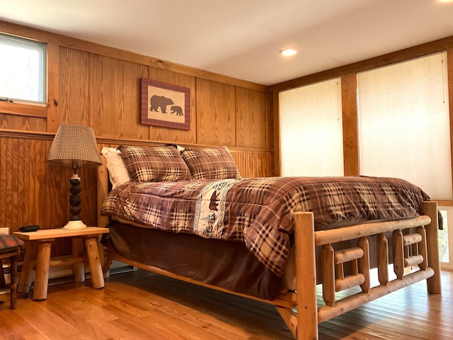 bedroom with wood walls, light hardwood / wood-style floors, and multiple windows