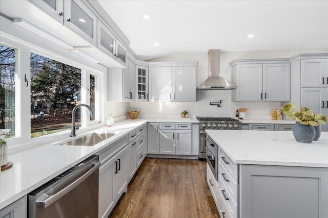 kitchen featuring dark wood-type flooring, wall chimney range hood, sink, light stone counters, and stainless steel appliances