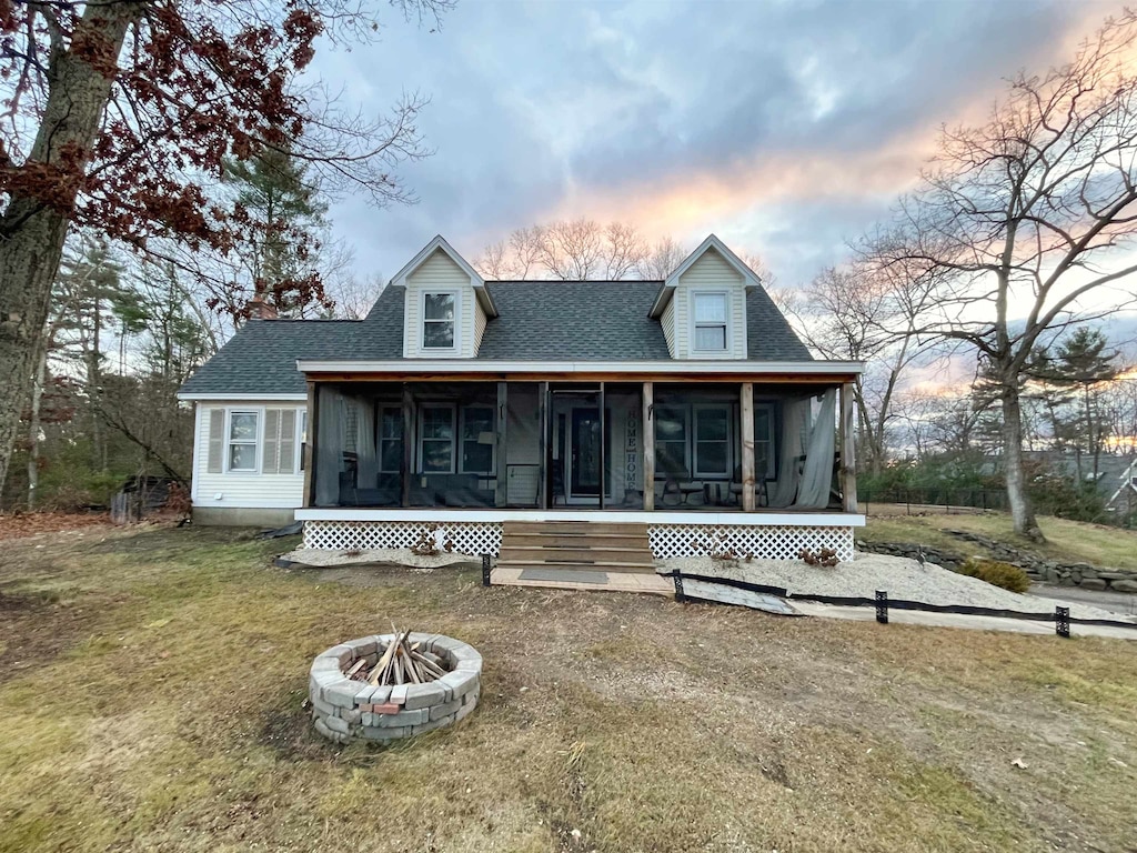 back house at dusk with a sunroom, a yard, and a fire pit