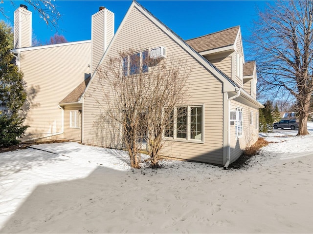 snow covered house featuring an AC wall unit