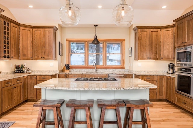 kitchen with a breakfast bar, hanging light fixtures, light hardwood / wood-style flooring, appliances with stainless steel finishes, and a kitchen island