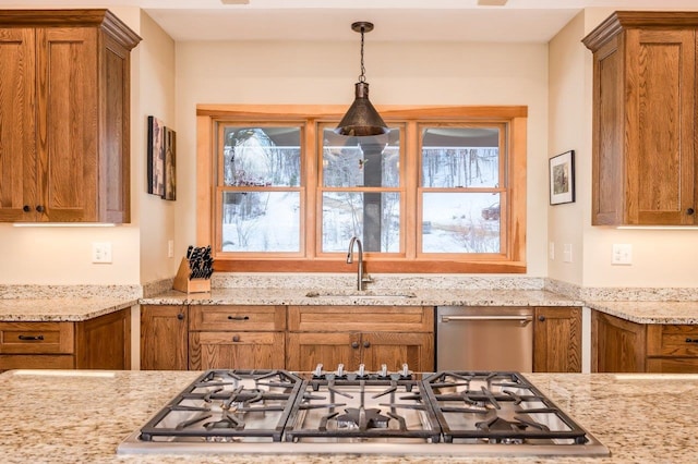 kitchen featuring light stone counters, sink, stainless steel appliances, and decorative light fixtures