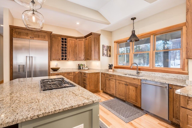 kitchen featuring pendant lighting, lofted ceiling, sink, light wood-type flooring, and appliances with stainless steel finishes