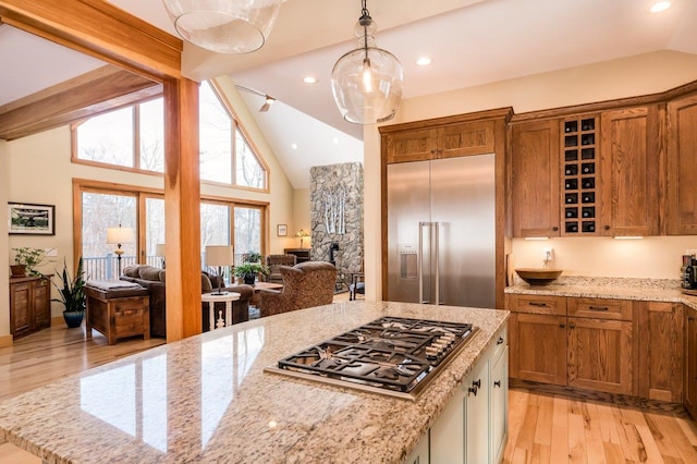 kitchen featuring light stone countertops, beam ceiling, appliances with stainless steel finishes, decorative light fixtures, and light hardwood / wood-style floors