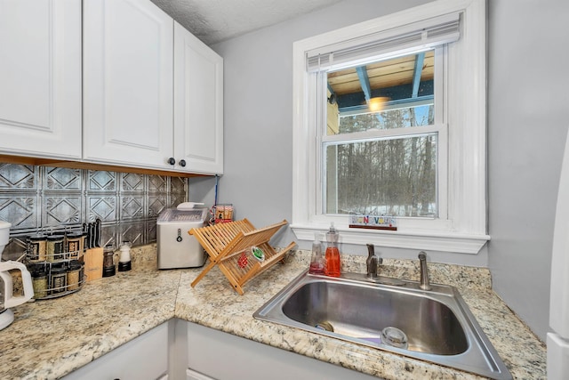 kitchen with light stone countertops, white cabinets, tasteful backsplash, and sink