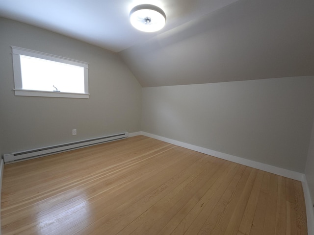 additional living space with a baseboard heating unit, vaulted ceiling, and light hardwood / wood-style flooring