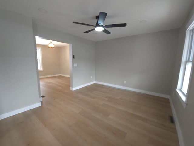 spare room with ceiling fan with notable chandelier and light wood-type flooring