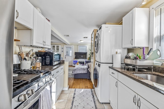 kitchen featuring dark stone counters, white cabinetry, stacked washer and dryer, and stainless steel appliances