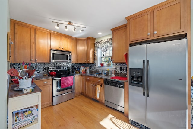 kitchen featuring dark stone counters, sink, light wood-type flooring, tasteful backsplash, and stainless steel appliances