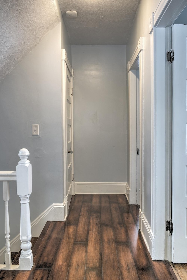 hall featuring a textured ceiling, dark hardwood / wood-style floors, and vaulted ceiling