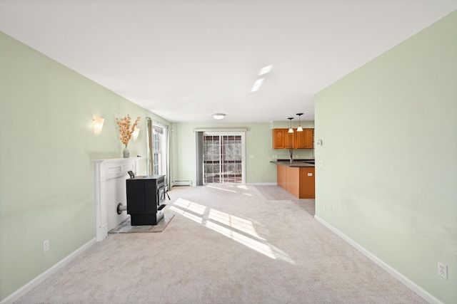 unfurnished living room with a wood stove, light colored carpet, and a baseboard heating unit