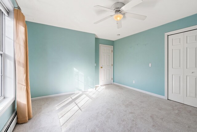 unfurnished bedroom with ceiling fan, baseboard heating, light colored carpet, multiple windows, and a closet