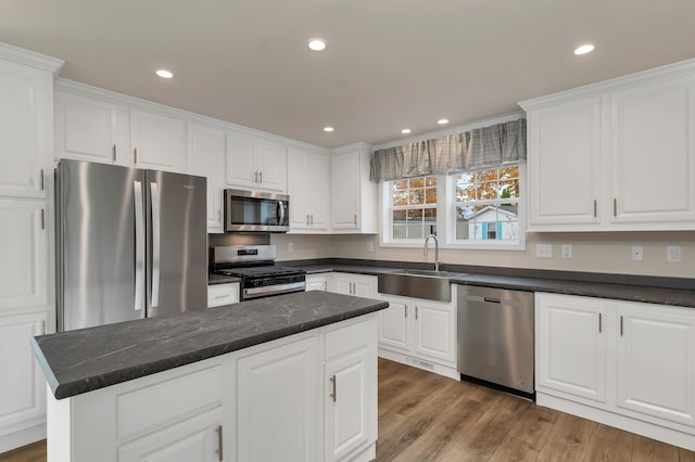 kitchen with hardwood / wood-style floors, white cabinets, sink, appliances with stainless steel finishes, and a kitchen island