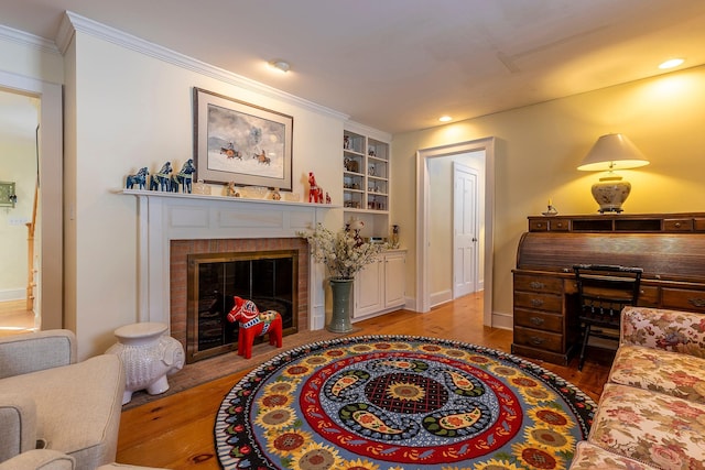 sitting room featuring built in shelves, a brick fireplace, ornamental molding, and hardwood / wood-style floors