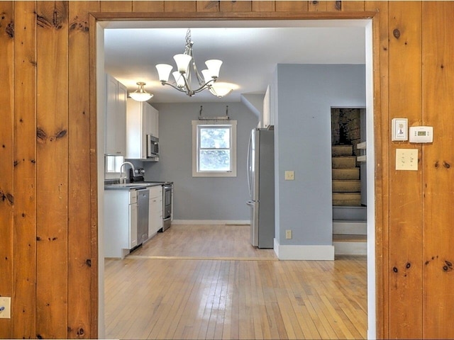 kitchen with white cabinetry, stainless steel appliances, a chandelier, decorative light fixtures, and light hardwood / wood-style floors