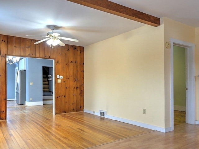 unfurnished room with beamed ceiling, light wood-type flooring, ceiling fan, and wood walls