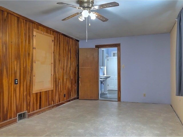 unfurnished room featuring ceiling fan and wood walls