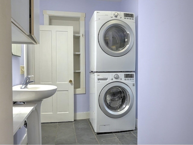 washroom with dark tile patterned floors, stacked washing maching and dryer, and sink