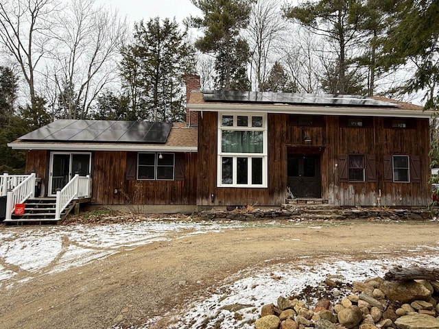 rear view of house featuring solar panels, a chimney, and entry steps