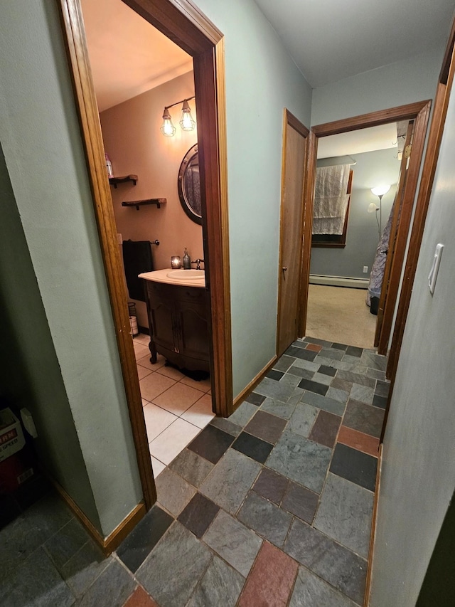 corridor featuring a sink, stone finish flooring, baseboards, and a baseboard radiator