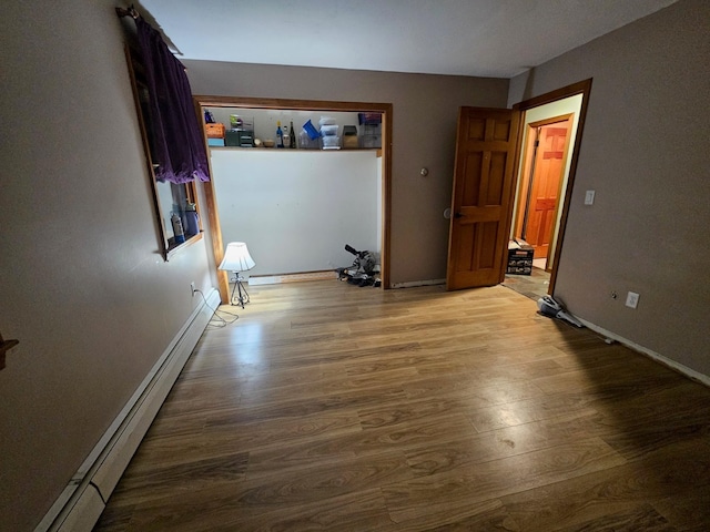 unfurnished bedroom with wood finished floors, baseboards, and baseboard heating