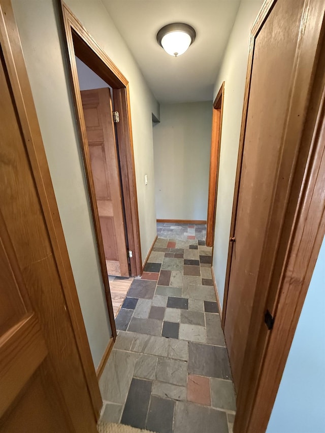 corridor with baseboards and stone tile flooring