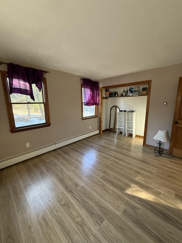 unfurnished living room featuring a baseboard heating unit, wood finished floors, and baseboards