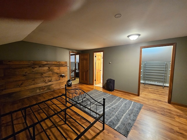 bedroom with a baseboard radiator, baseboards, lofted ceiling, and wood finished floors