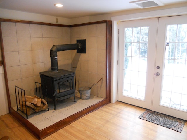 doorway to outside featuring french doors, light hardwood / wood-style floors, a wood stove, and tile walls