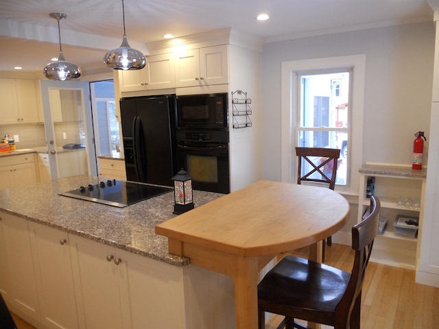 kitchen featuring light stone countertops, hanging light fixtures, light hardwood / wood-style floors, white cabinets, and black appliances