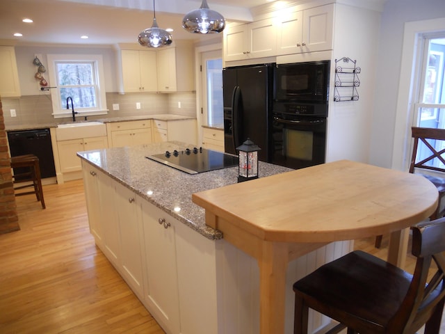 kitchen with sink, hanging light fixtures, tasteful backsplash, white cabinets, and black appliances