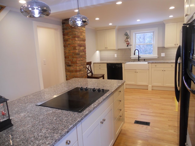 kitchen with sink, hanging light fixtures, light hardwood / wood-style flooring, stone countertops, and black appliances