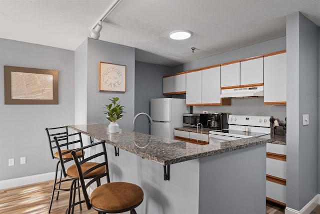 kitchen featuring white cabinetry, rail lighting, white appliances, a kitchen bar, and light wood-type flooring