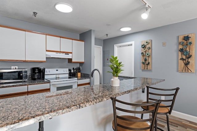 kitchen with white cabinets, white electric range oven, a kitchen bar, and light wood-type flooring