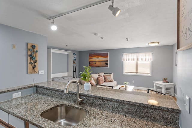 kitchen with stone counters, sink, rail lighting, and a textured ceiling