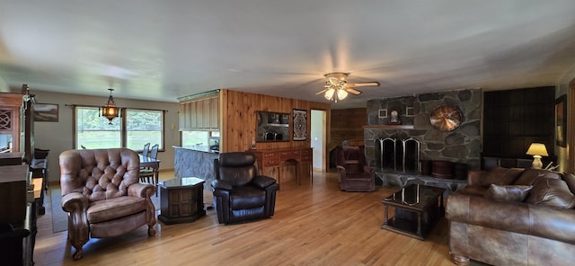 living room featuring light hardwood / wood-style floors, a stone fireplace, and ceiling fan