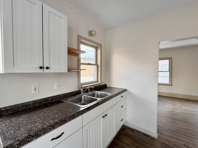 kitchen with white cabinets, dark hardwood / wood-style flooring, dark stone countertops, and sink