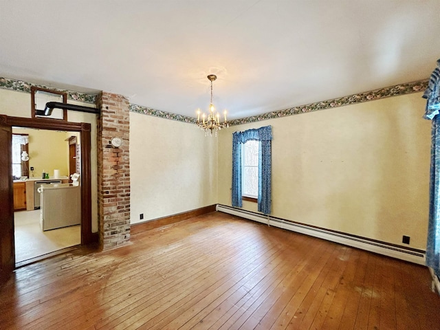 empty room with an inviting chandelier, baseboard heating, and light hardwood / wood-style flooring