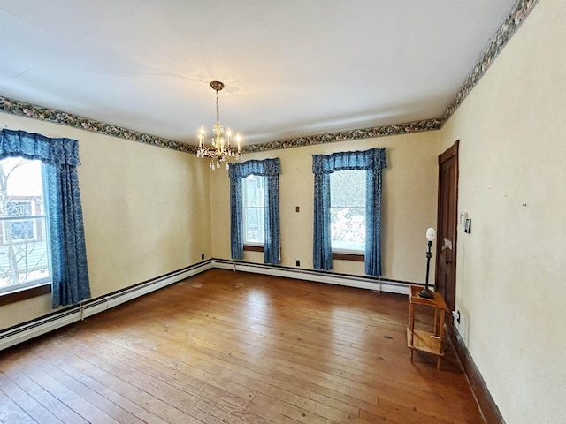 empty room featuring hardwood / wood-style flooring, a baseboard radiator, and an inviting chandelier