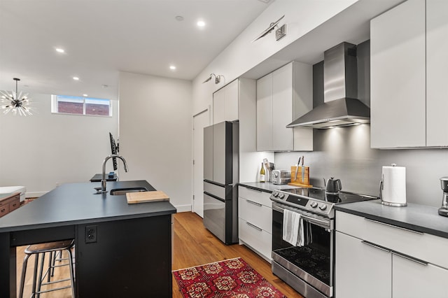 131 Main St Unit 2A-1, Burlington, VT 05401 - kitchen featuring appliances with stainless steel finishes, wall chimney exhaust hood, a kitchen island with sink, dark countertops, and light wood finished floors
