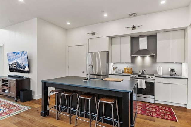 131 Main St Unit 2A-1, Burlington, VT 05401 - kitchen featuring wall chimney range hood, appliances with stainless steel finishes, dark countertops, a breakfast bar area, and light wood finished floors