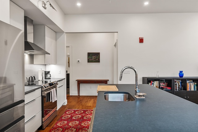 131 Main St Unit 2A-1, Burlington, VT 05401 - kitchen with wall chimney exhaust hood, stainless steel appliances, dark wood finished floors, white cabinets, and dark countertops