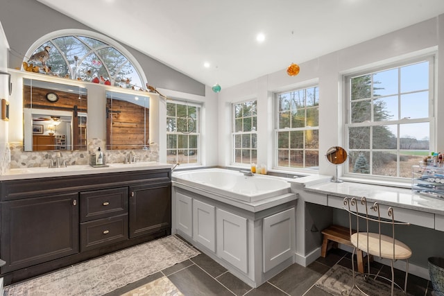 bathroom with decorative backsplash, a healthy amount of sunlight, vanity, and vaulted ceiling