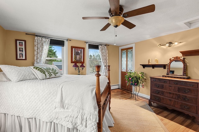 bedroom with ceiling fan, a baseboard heating unit, a textured ceiling, and light hardwood / wood-style flooring