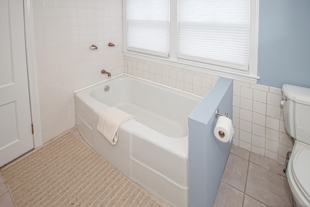 bathroom featuring tile patterned flooring, a tub to relax in, toilet, and tile walls