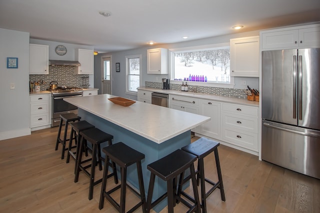 kitchen featuring a breakfast bar, hardwood / wood-style flooring, a kitchen island, white cabinetry, and stainless steel appliances