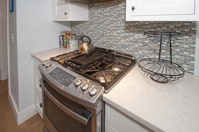 kitchen with white cabinets, stainless steel gas stove, tasteful backsplash, and light hardwood / wood-style flooring