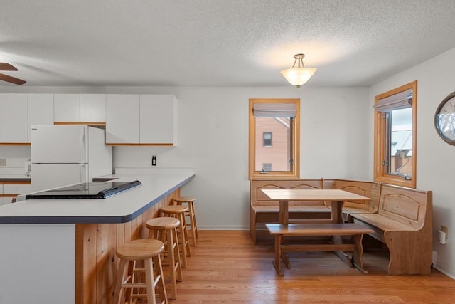 kitchen featuring kitchen peninsula, a textured ceiling, light hardwood / wood-style flooring, white fridge, and white cabinetry