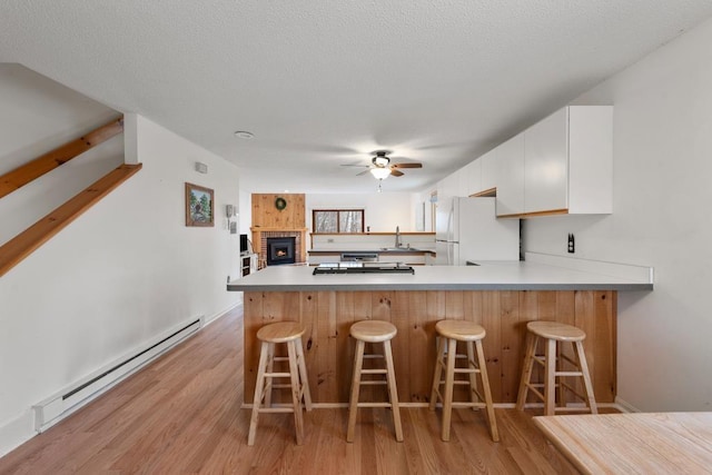 kitchen with kitchen peninsula, light hardwood / wood-style flooring, baseboard heating, white fridge, and white cabinetry