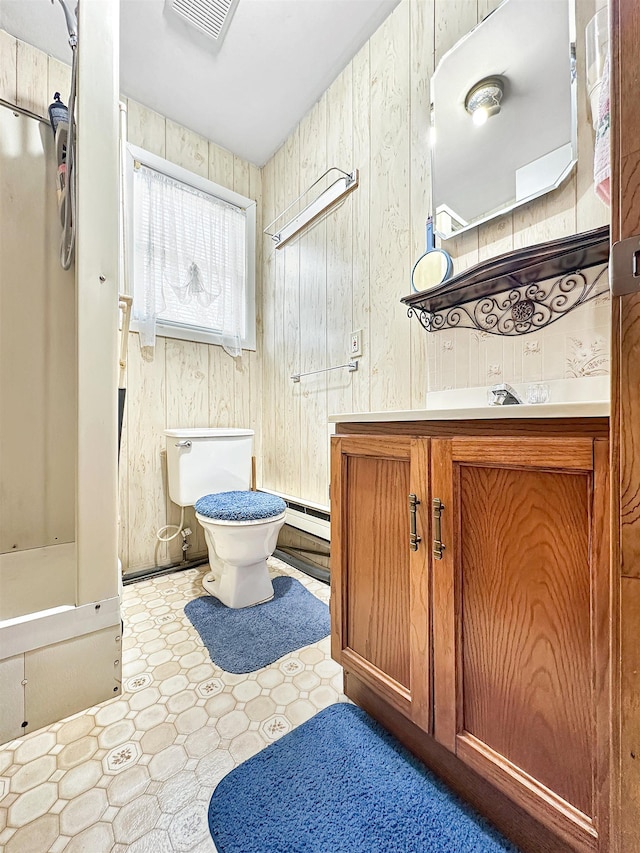 bathroom featuring wood walls, vanity, a baseboard heating unit, and toilet